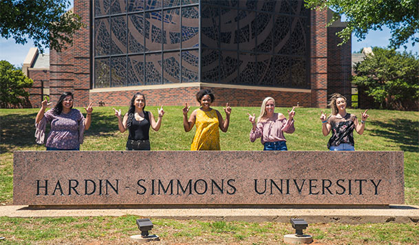 Group of female students standing behind university sign